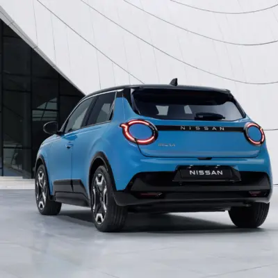 hero-shot-rear-7_8-view-of-new-Micra-in-blue-gear-color-in-front-of-a-white-blue-design-architectural-building-scaled